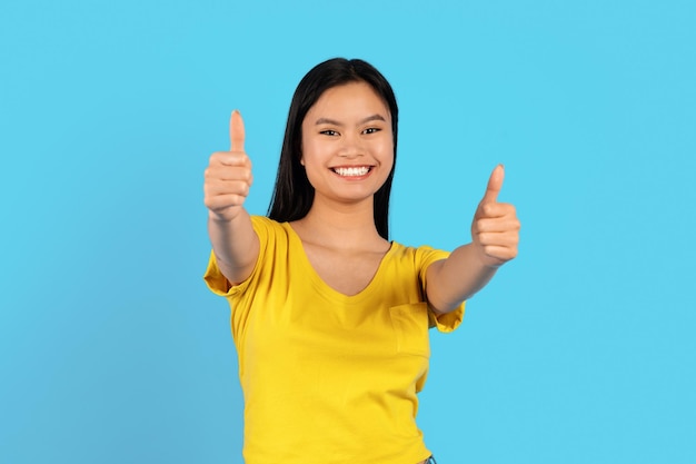 Portrait of cheerful pretty young chinese woman in yellow tshirt show thumbs up gesture recommend ad