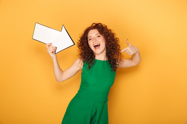 Portrait of a cheerful redhead woman in dress pointing away