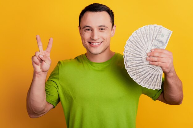 Foto il ritratto del ragazzo ricco allegro mostra il fan dei soldi della tenuta del v-segno su fondo giallo