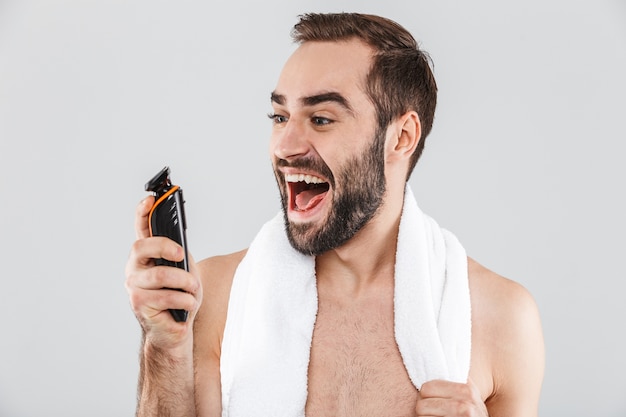 Portrait of a cheerful shirtless bearded man showing electric razor isolated over white