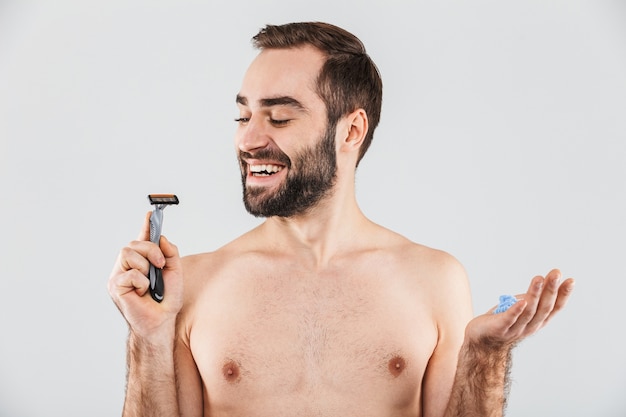 Portrait of a cheerful shirtless bearded man standing isolated over white, holding razor