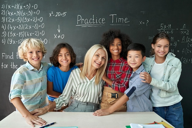 Portrait of cheerful smiling teacher and diverse schoolkids near chalkboard