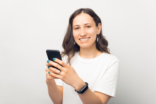 Portrait of cheerful smiling young beautiful woman holding smartphone and looking at camera