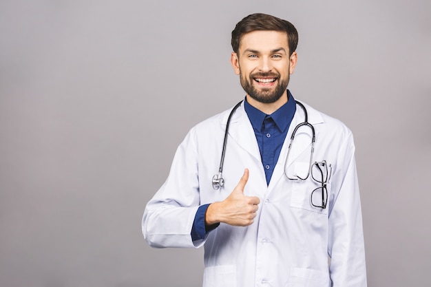 Ritratto di giovane medico sorridente allegro con lo stetoscopio sopra il collo in cappotto medico pollici in su.