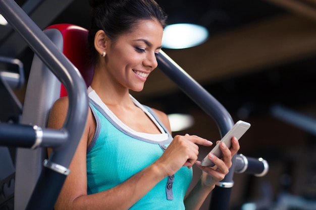 Portrait of a cheerful sports woman using smartphone in fitness gym