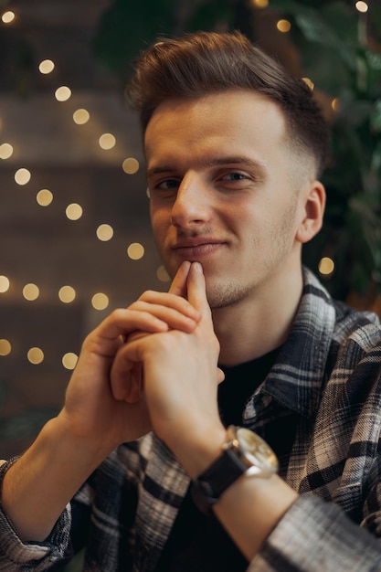 Portrait of cheerful stylish male freelancer in plaid shirt looking at camera with hands at chin