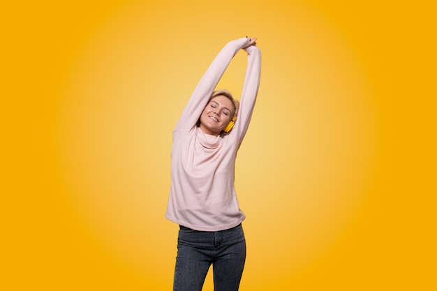 Photo portrait of a cheerful stylish young woman standing isolated over yellow background listening to music with headphones dancing