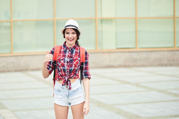 Portrait of a cheerful tourist girl showing thumb up in the city