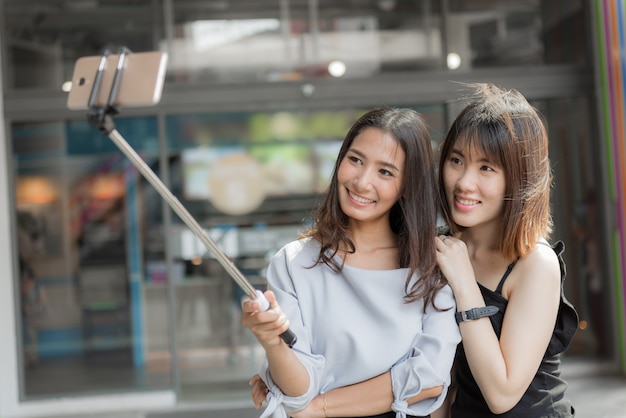 Photo portrait of cheerful two smiling girlfriends making a selfie at shopping mall.