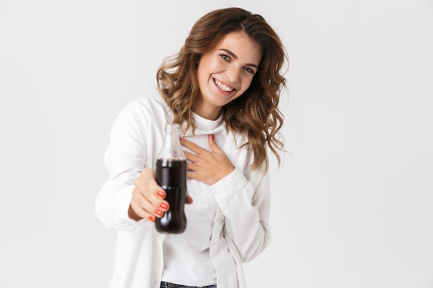 Portrait of cheerful woman in casual clothes holding bottle with soda while standing, isolated