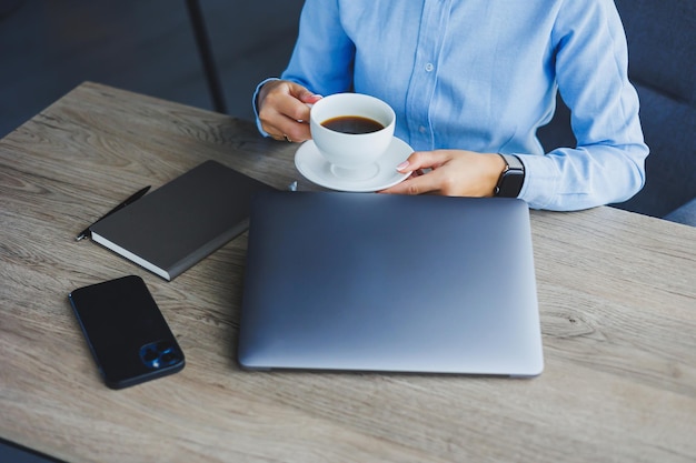 Ritratto di donna allegra con gli occhiali classici che sorride nel tempo libero nella caffetteria con caffè donna europea positiva in camicia blu scrivania con laptop lavoro a distanza