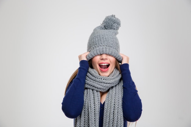 Ritratto di una donna allegra che si copre gli occhi con un cappello isolato su un muro bianco