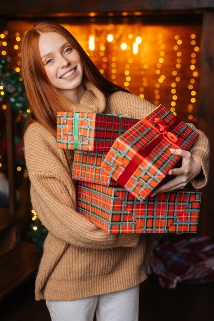 Portrait of cheerful woman holding many beautiful Christmas gift boxes on background of xmas lights