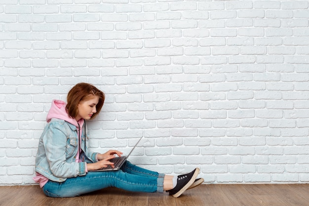 Ritratto di una donna allegra che si siede sul pavimento con il computer portatile