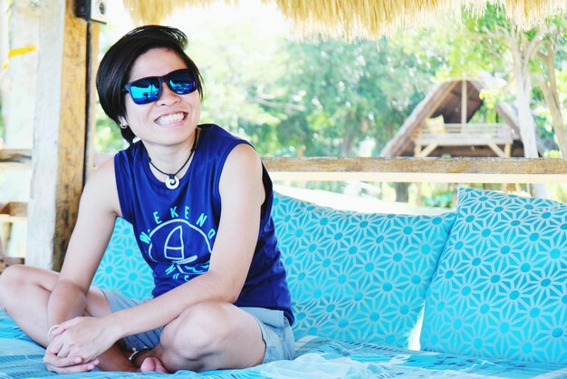 Photo portrait of cheerful woman wearing sunglasses while sitting on sofa