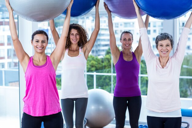 Portrait of cheerful women holding exercise balls with arms raised 