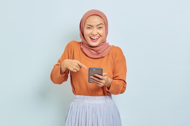 Portrait of cheerful young Asian Muslim woman in brown sweater and hijab using mobile phone isolated on white background Muslim lifestyle concept