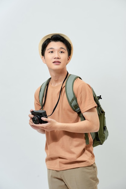Portrait of cheerful young Asian tourist man holding digital camera and taking photo when standing