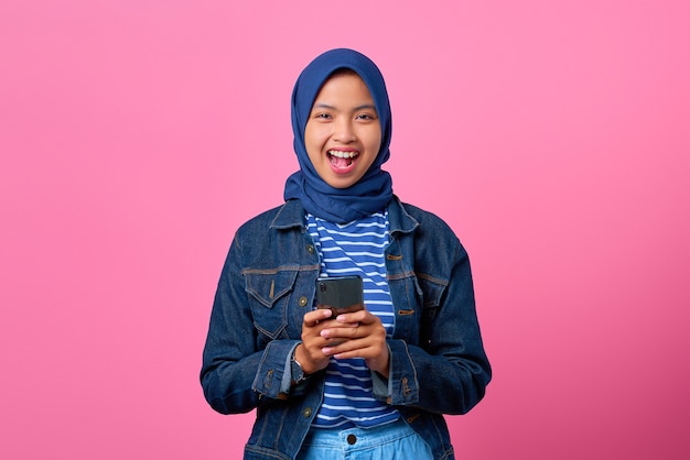 Portrait of cheerful young Asian woman holding smartphone while looking at camera