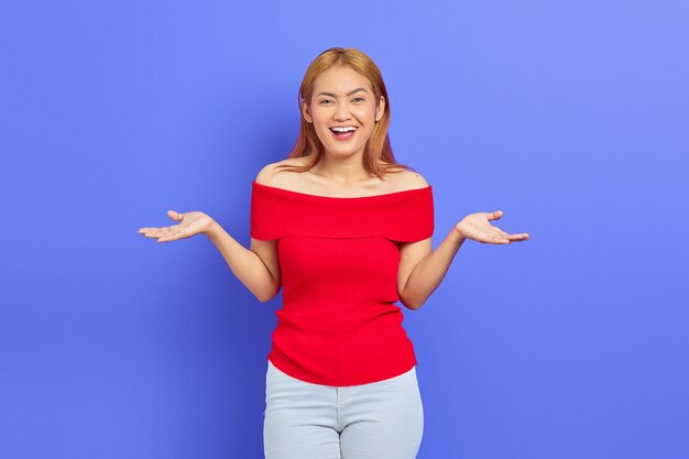 Portrait of cheerful young Asian woman with hand gesture inviting to come isolated on purple background