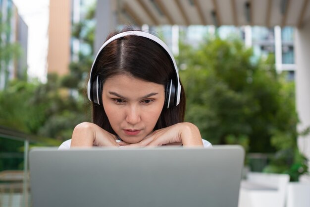 Portrait of a cheerful young attractive Asian woman listening music and using laptop computer for working online Distance learning online education and work via the internet Successful people