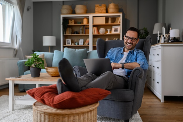 Portrait of cheerful young businessman laughing and doing research over laptop