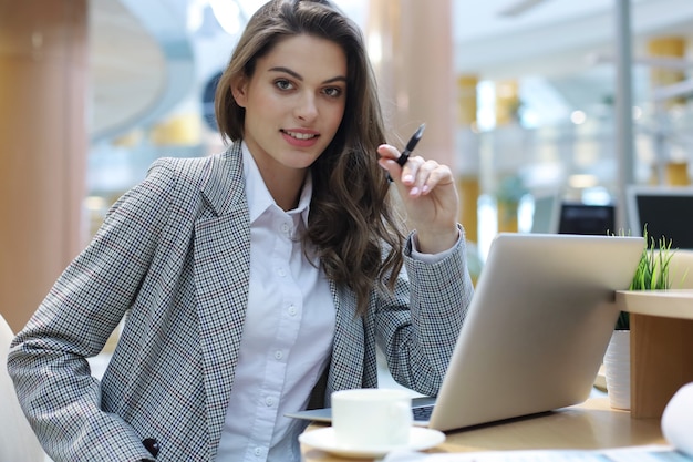 Portrait of a cheerful young businesswoman sitting at the table in office and looking at camera.