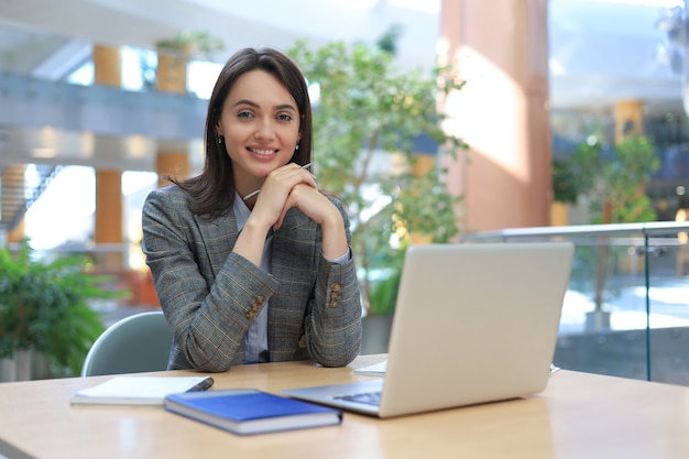 portrait of a cheerful young businesswoman sitting at the table in office and looking at camera.