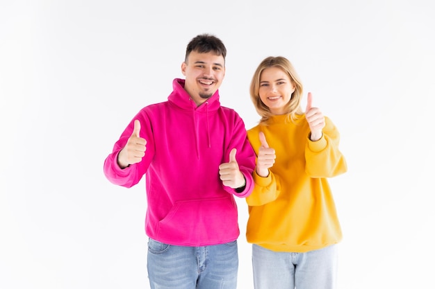 Portrait of a cheerful young couple wearing hoodies standing isolated over white background ok gest