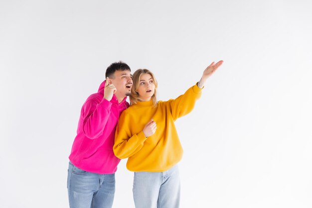 Portrait of a cheerful young couple wearing hoodies standing isolated over white background ok gest