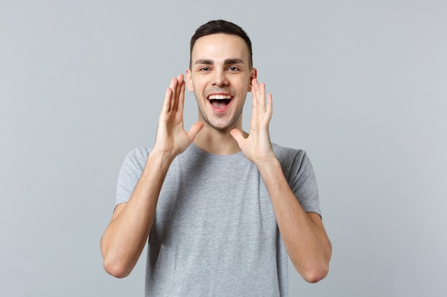 Portrait of cheerful young man in casual clothes screaming with hands gesture near mouth 