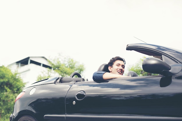 portrait of cheerful young man driving car against clear sky