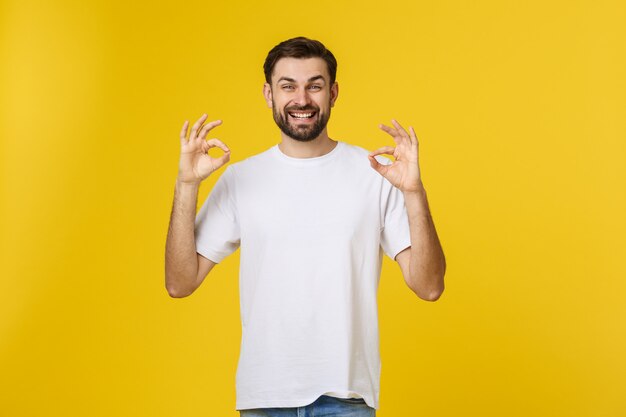 Портрет жизнерадостного молодого человека показывая одобренный жест изолированный на желтом цвете