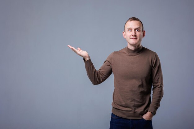 Portrait of cheerful young man smiling while looking at camera pointing with finger on gray background