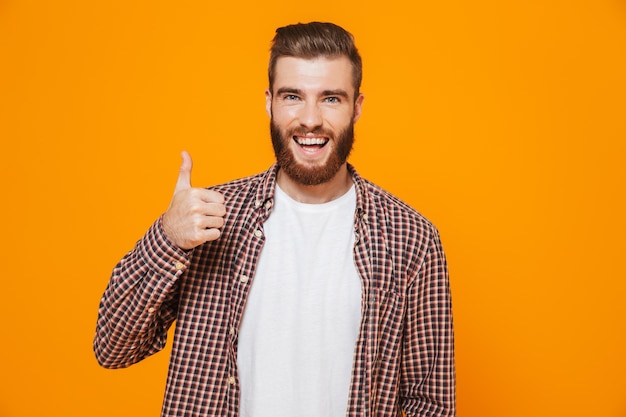 Portrait of a cheerful young man wearing casual clothes standing isolated over yellow wall, giving thumbs up