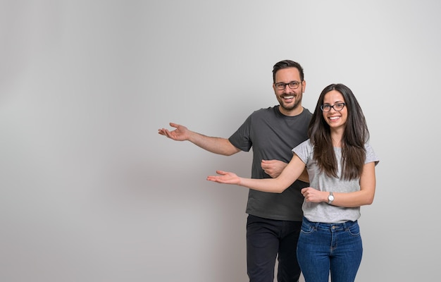 Portrait of cheerful young man and woman gesturing at copy space for advertisement