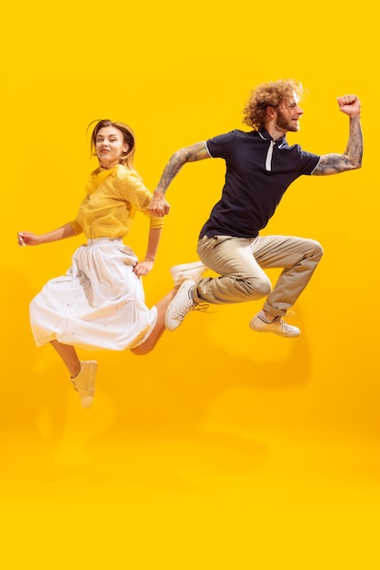 Portrait of cheerful young man and woman posing in a jump isolated over yellow studio background