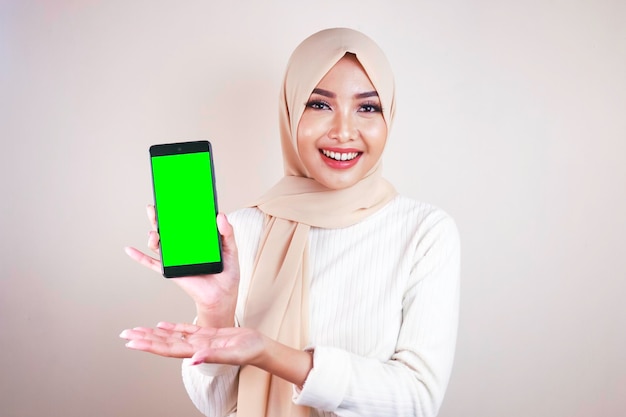 緑の画面で携帯電話を指している陽気な若いイスラム教徒のアジアの女性の肖像画