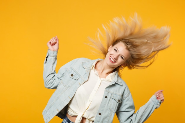 Photo portrait of cheerful young woman in denim casual clothes with flying hair having fun, looking camera isolated on yellow orange wall background in studio. people lifestyle concept. mock up copy space.