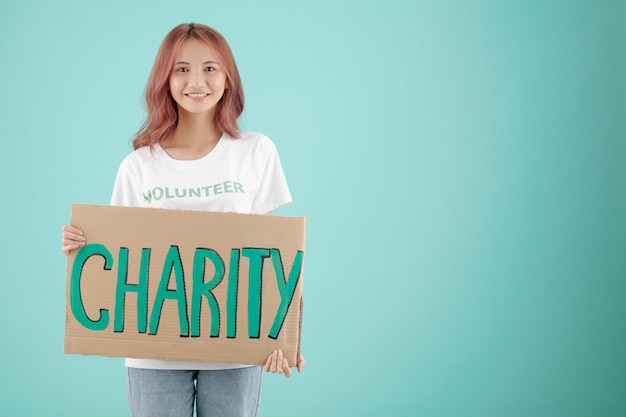 Photo portrait of cheerful young woman holding charity placard, isolated on turquoise