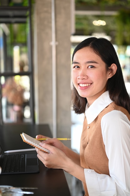 Portrait of cheerful young woman holding notebook and smiling