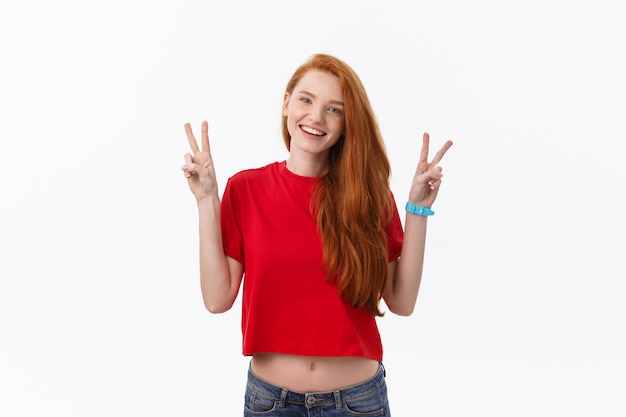 Photo portrait of cheerful young woman showing two fingers or victory gesture, over grey