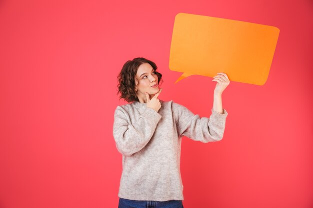 Portrait of a cheerful young woman standing isolated over pink, holding empty speech bubble