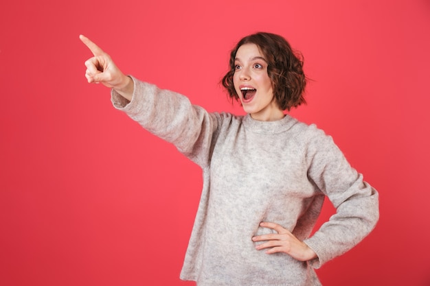 Portrait of a cheerful young woman standing isolated over pink, presenting copy space