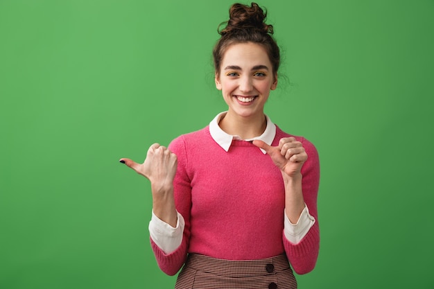 Portrait of a cheerful young woman standing isolated, pointing at copy space