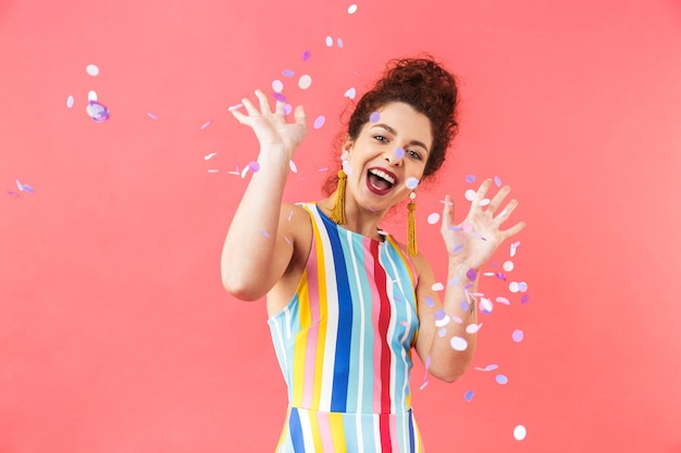 Portrait of a cheerful young woman wearing dress standing isolated over red background