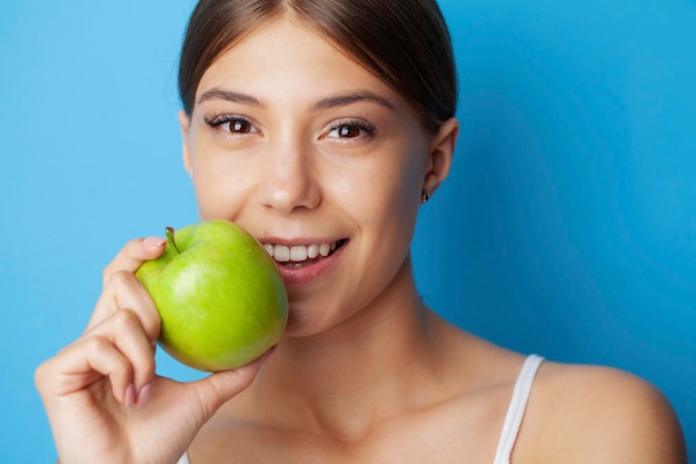 Portrait of a cheerful young woman with perfect smile eating green apple.