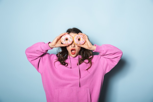 Foto ritratto di giovane donna allegra con due code di cavallo sorridente mentre si tengono ciambelle dolci sopra l'azzurro in studio