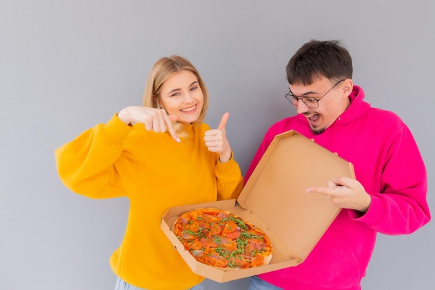 Portrait of cheery couple man and woman in colored sweaters smiling while eating pizza
