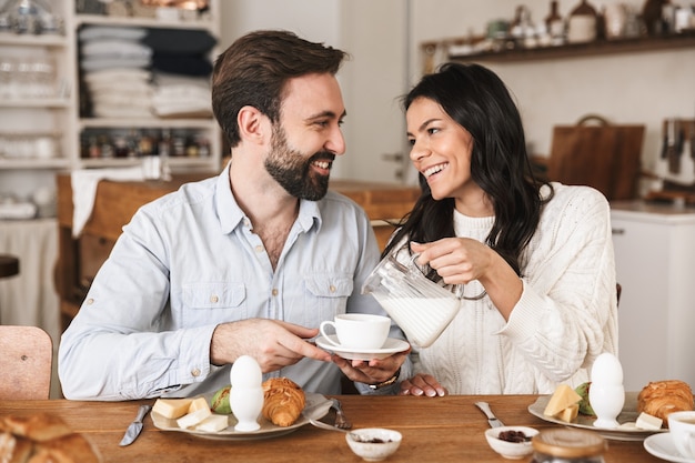 自宅のキッチンで朝食をしながらコーヒーを飲む陽気なヨーロッパのカップルの男性と女性の肖像画